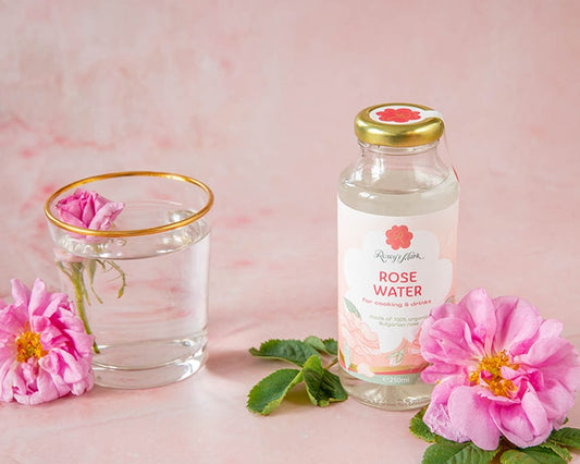 Rosey's Mark Rosenwasser 250ml aus Bulgarien, stilvoll mit Glas und frischen Rosenblüten arrangiert, perfekt für Getränke und feine Küche.