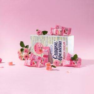Mini-Lokum mit Rosengeschmack - Bulgarien | Süße Zeiten 30g, dekorativ arrangiert mit Rosenblüten vor Produktkarton, perfekt als Geschenkidee.