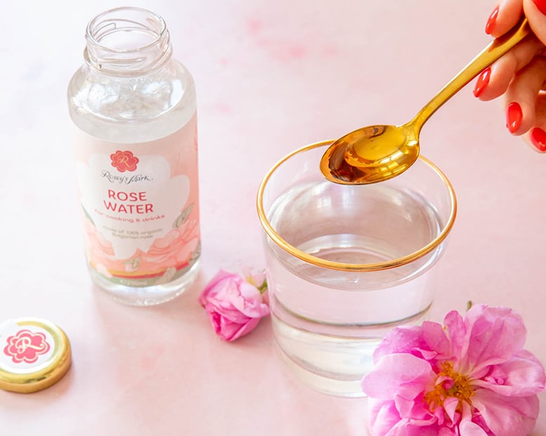 Bulgarisches Rosenwasser zum Kochen und Trinken 250ml von Rosey's Mark, mit goldener Teelöffel-Dosierung in Glas serviert, ideal für kulinarische Anwendungen.